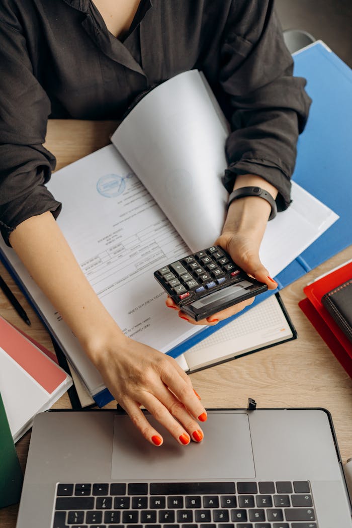 about-us-02 A business professional uses a calculator among documents and laptop on a desk for financial tasks.